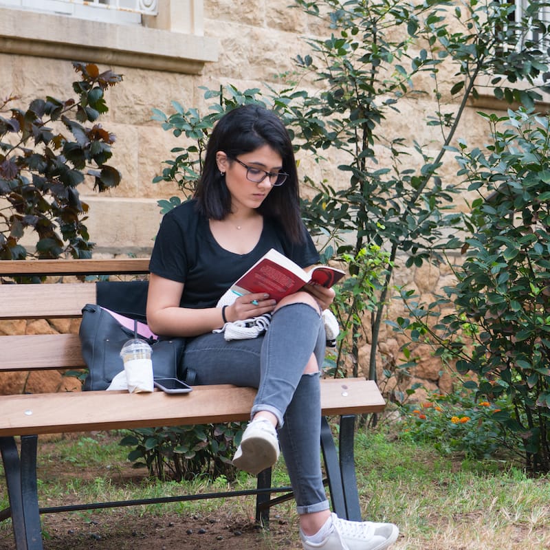 Cybersecurity student on park bench with coffee and text books